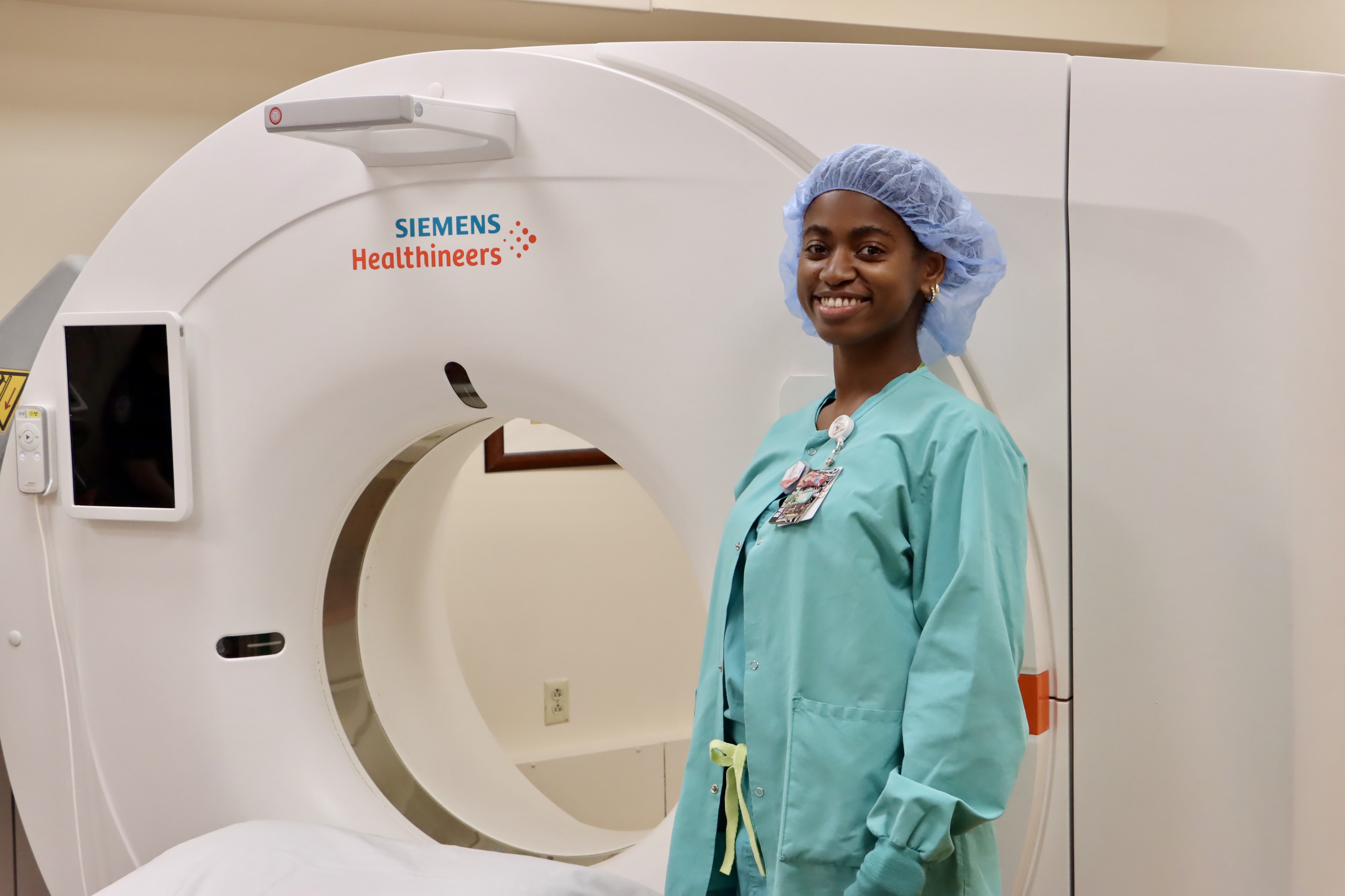 Smiling sonography student in scrubs standing next to an imaging machine