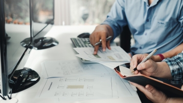 image of two people taking notes in front of two computer screens